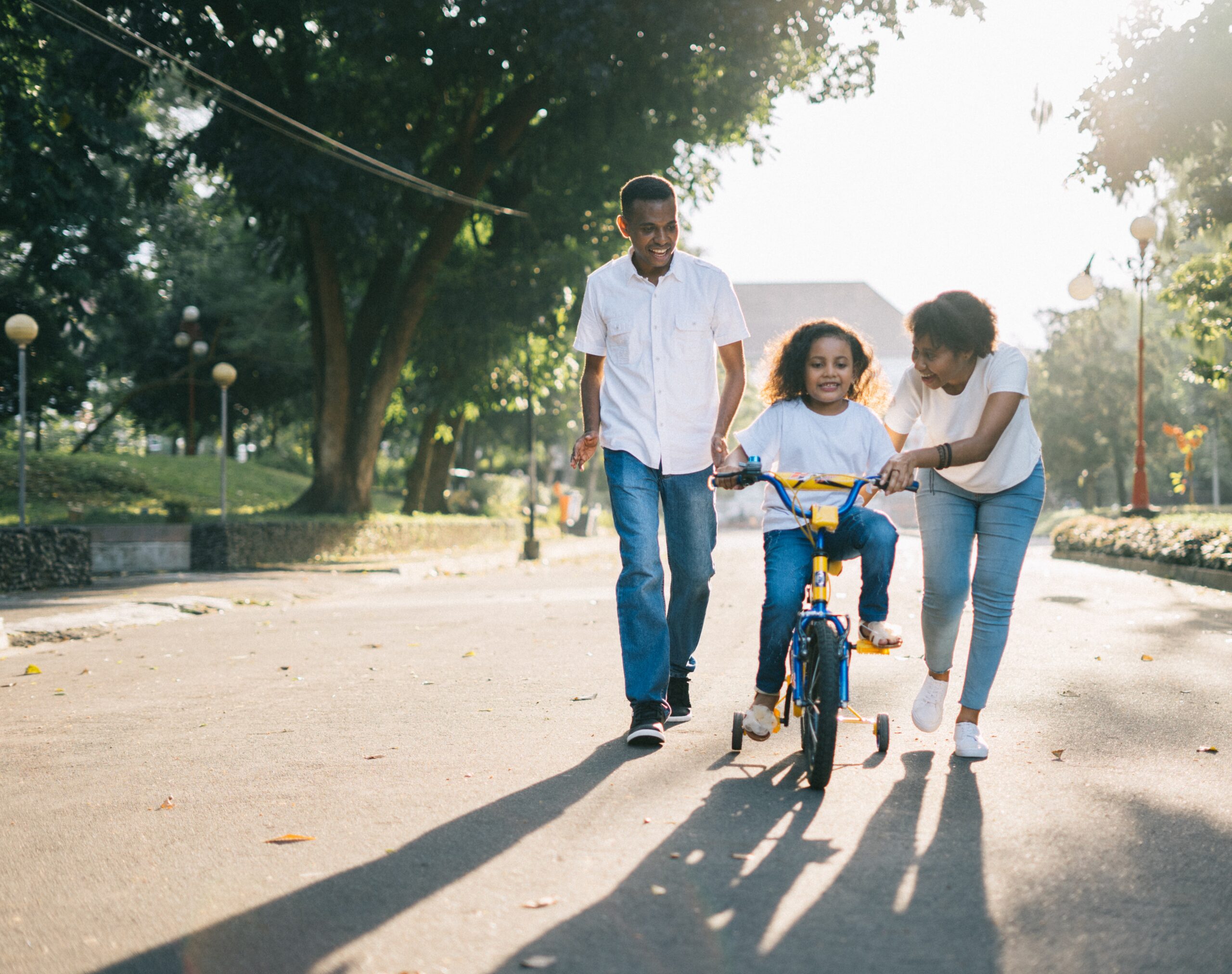 father teaching his kids how to ride a bike with training wheels