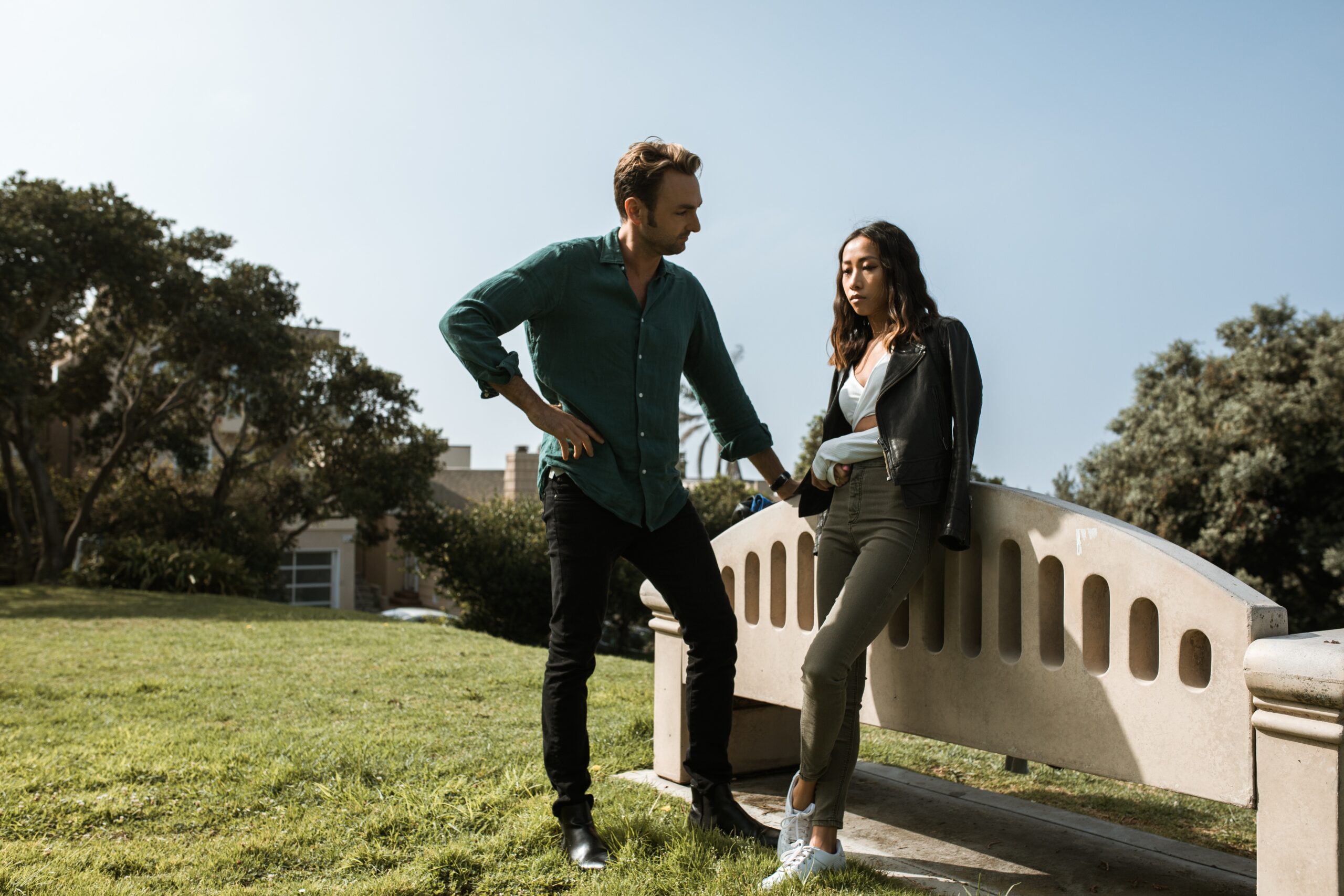 unhappy man standing by unhappy woman sitting on bench back