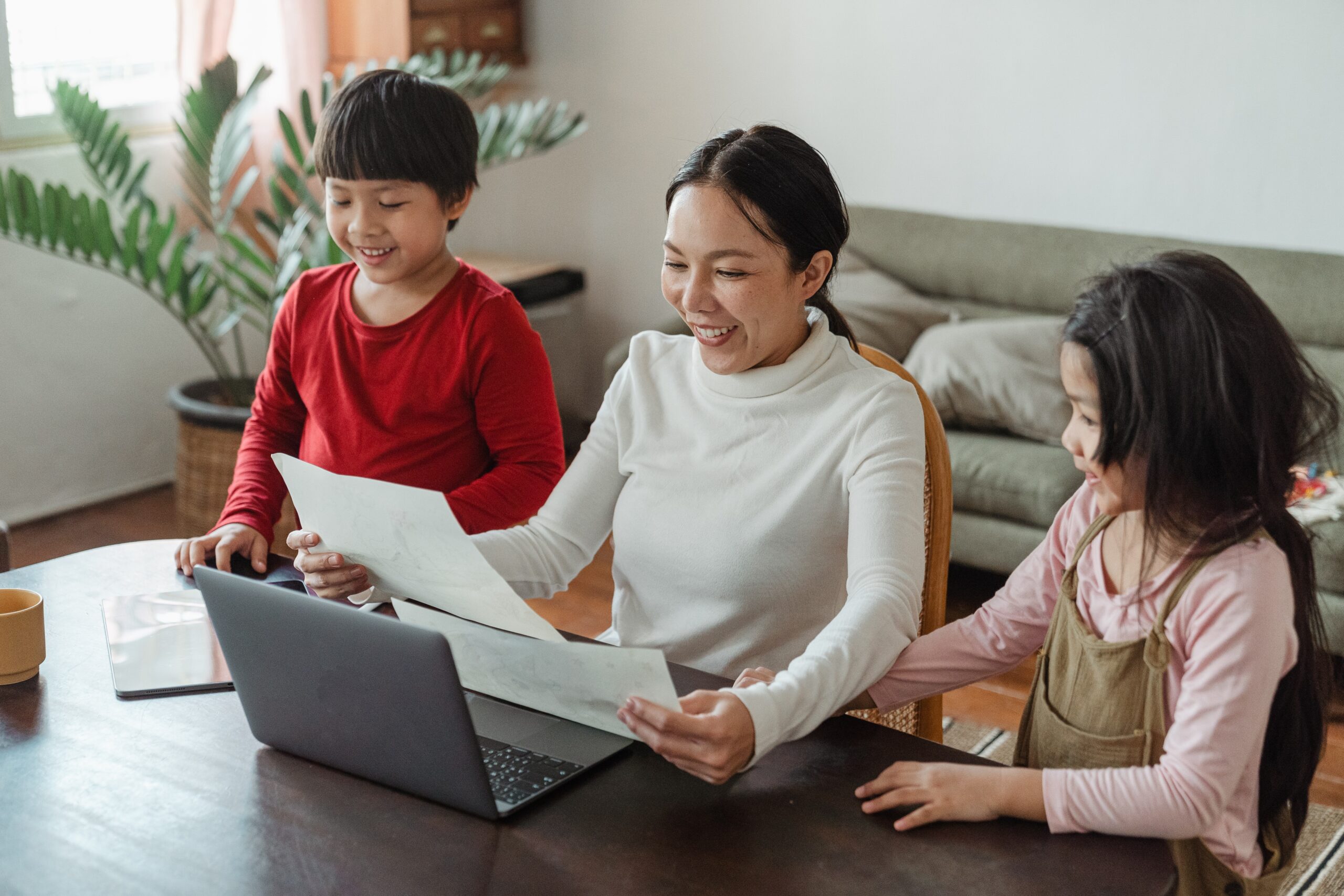 asian woman at laptop holding papers with a child on either side of her