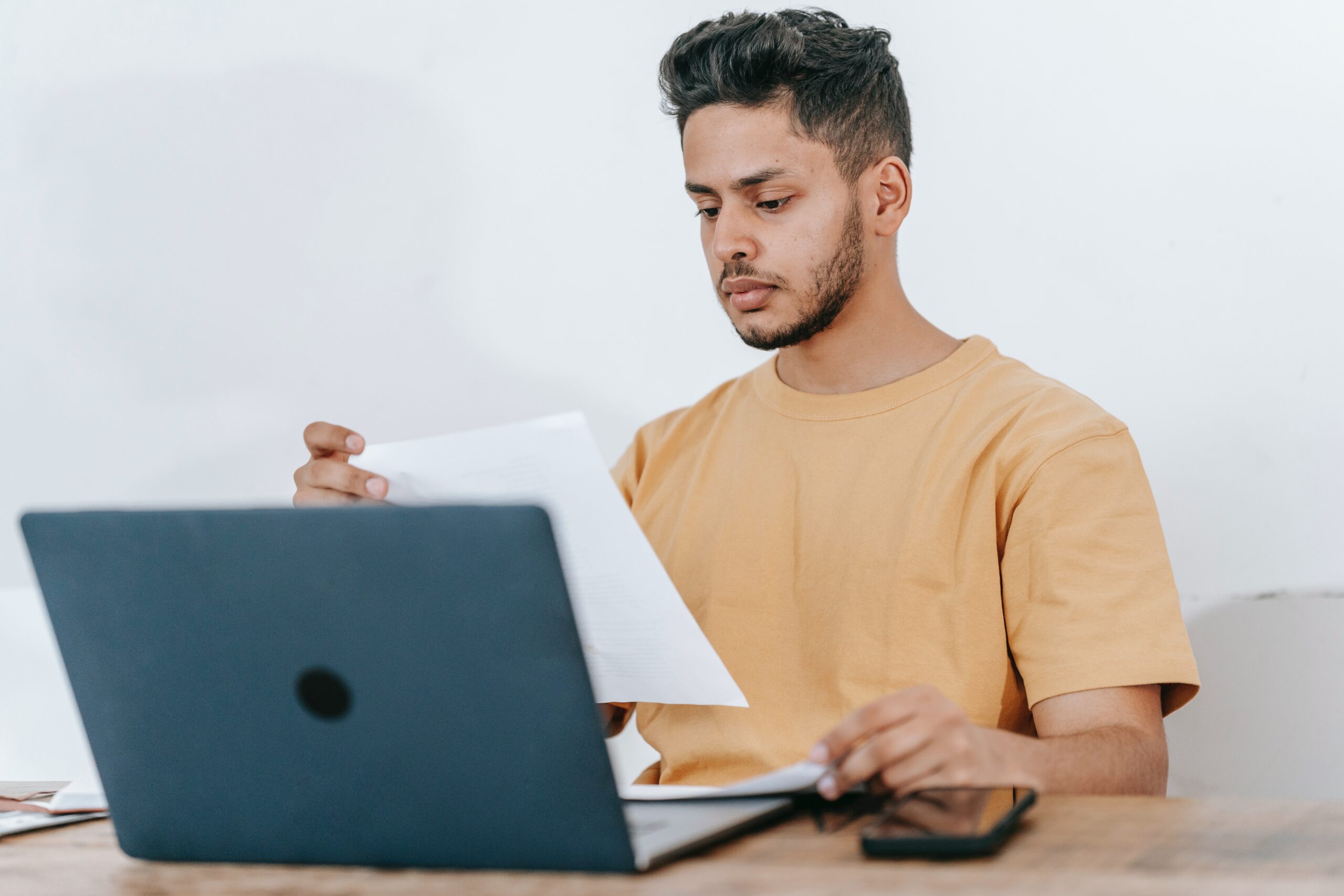 man sitting at table looking at papers in front of a laptop