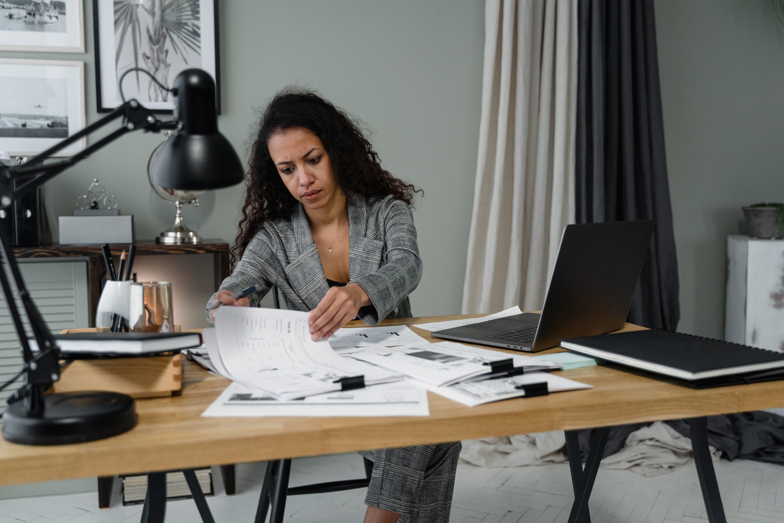 woman sitting at a desk with stacks of papers and a laptop