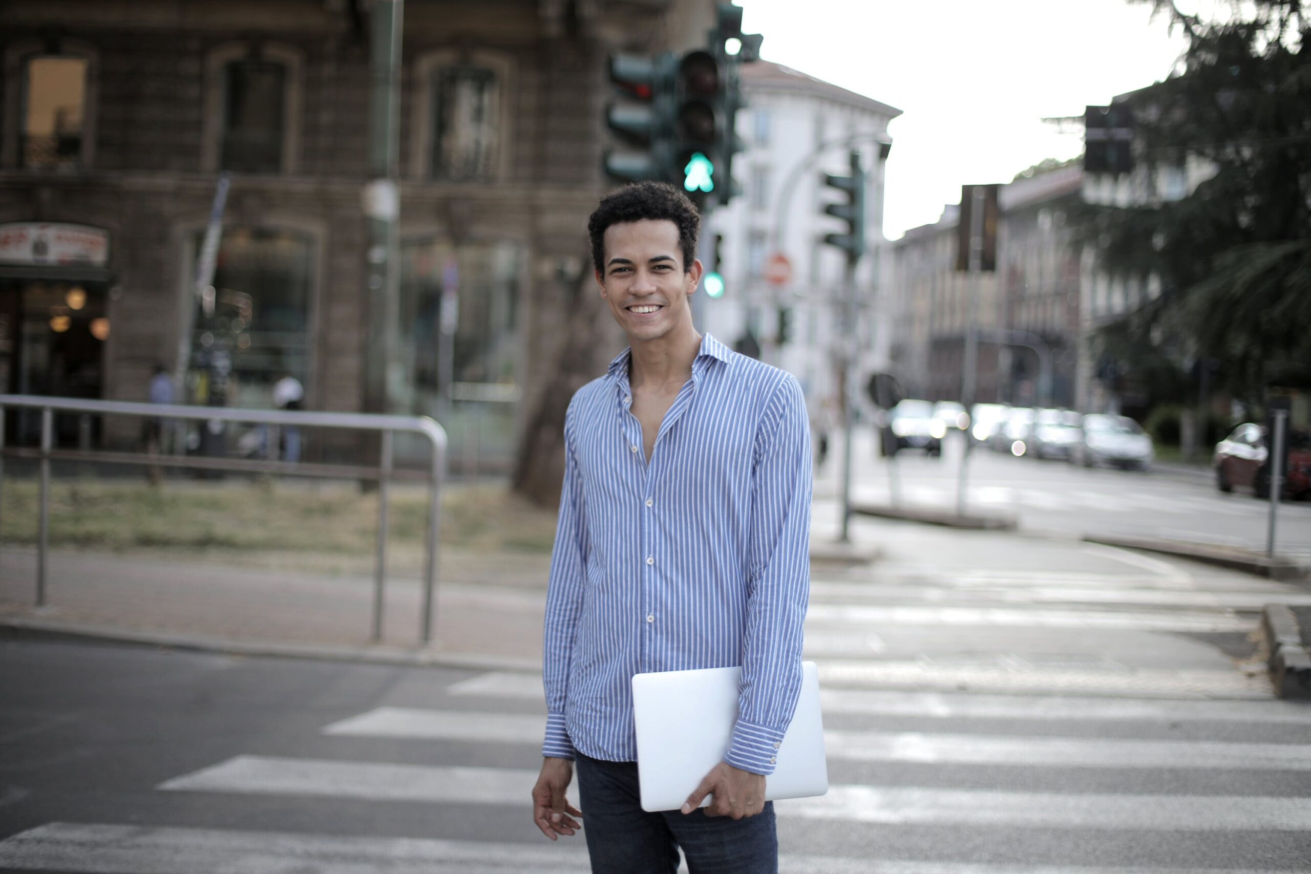 man holding laptop walking in a crosswalk